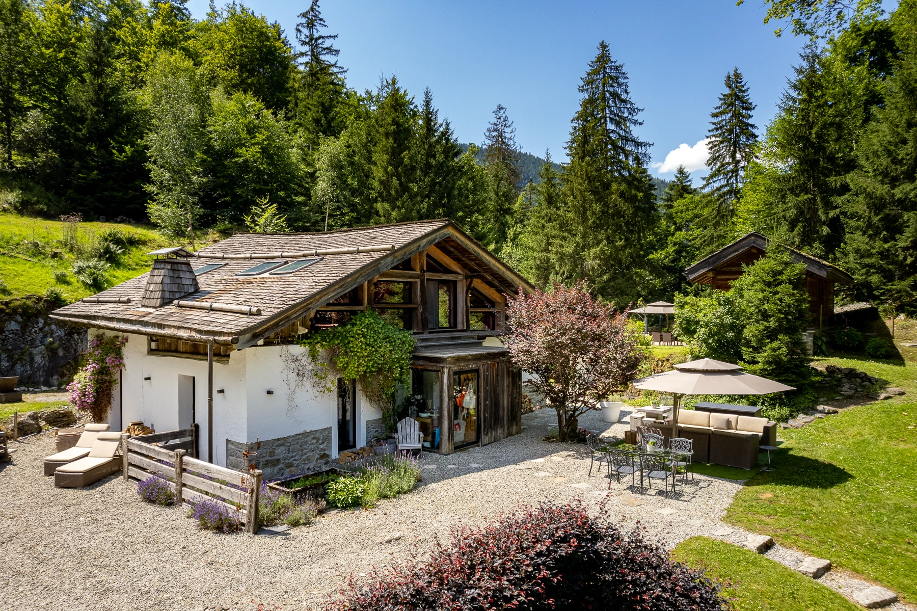 Photo du devant du chalet, terrasse de graviers, table à manger et salon d'extérieur