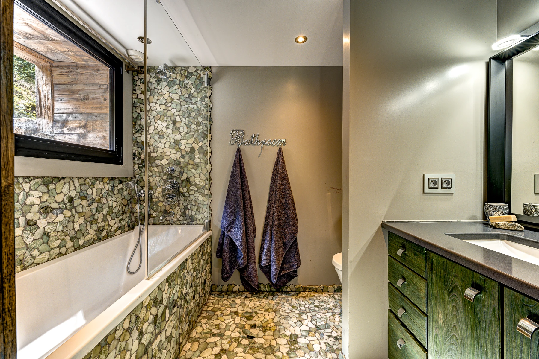 Photo de la salle de bain privative de la première chambre. Baignoire, galets, couleurs vert et anthracite