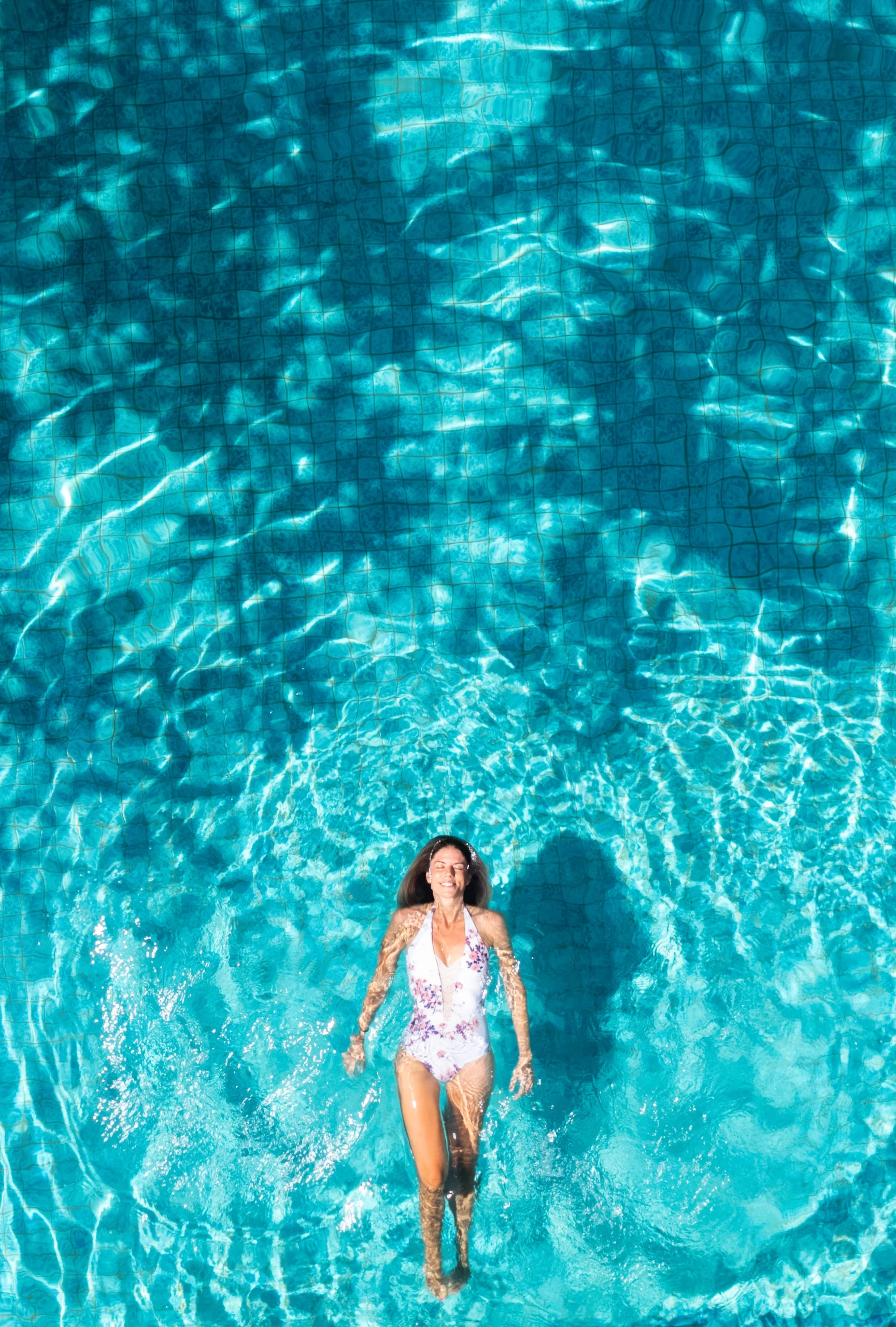 Photo drone d'une femme qui nage sur le dos dans une piscine à l'eau bleue claire